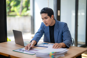 Fototapeta premium A man is sitting at a desk with a laptop and a stack of papers