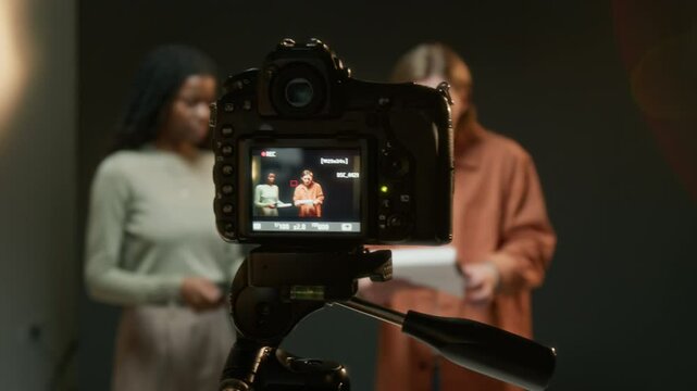 Close-up shot of camera recording two actors reading scripts while rehearsing their roles on set in studio
