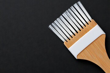 An artisan brush, characterized by its wooden handle and fine bristles, lies on a textured black surface, ideal for a range of painting and craft applications
