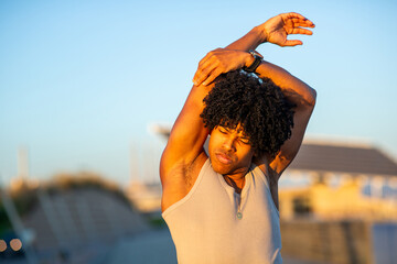 Focused young man with black curly hair doing arm stretch in sunlight outdoors