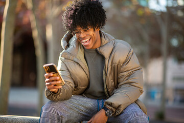Young man laughing while looking at smartphone outdoors