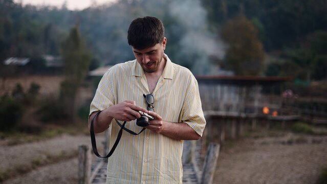Young man reviewing pictures on his analog camera during a journey in a remote village