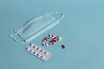 on a blue background, a medical mask, a white blister, and pills, the concept of a cold, and a...