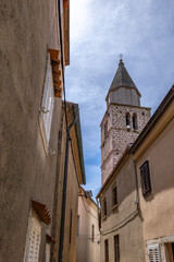 Walking among the monuments of the old town of Vrbnik, a tall tower with a clock in the center of...