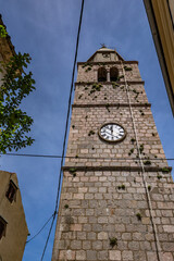 Walking among the monuments of the old town of Vrbnik, a tall tower with a clock in the center of...
