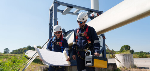 An engineer carefully examines a wind turbine blade at a construction site, placing a large blade...