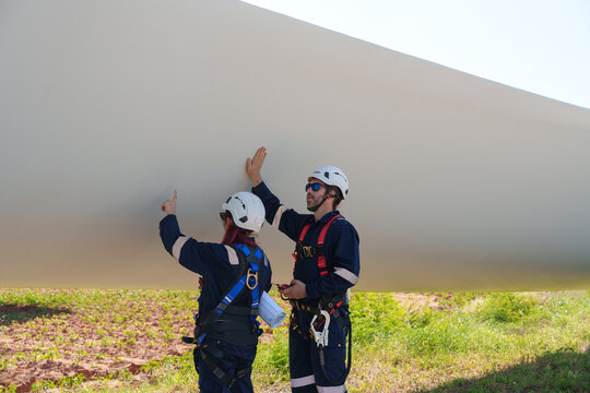 An engineer carefully examines a wind turbine blade at a construction site, placing a large blade on the ground to highlight the renewable energy technology. - Powered by Adobe