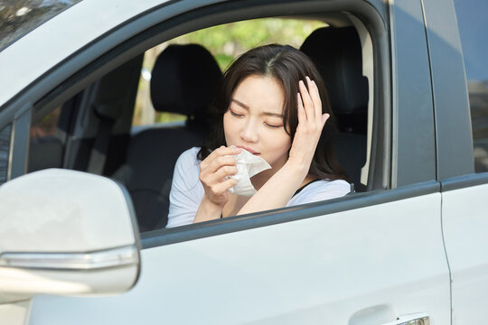 Young Woman Feeling Sick and Covering Mouth with Tissue in Car Interior on Sunny Day