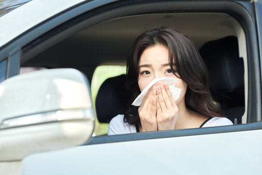Young Woman Feeling Sick and Covering Mouth with Tissue in Car Interior on Sunny Day
