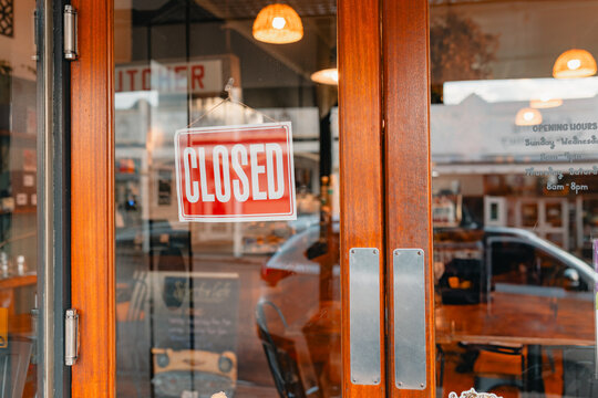 Vibrant red 'Closed' sign on front door of cafe in small town
