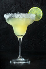 Margarita cocktail in the classic glass, side view on a black background, with a lime garnish and a...