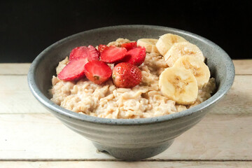a bowl of oatmeal with strawberries and bananas on top, on a wooden table
