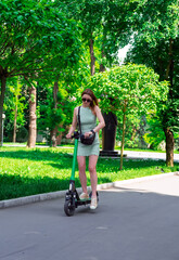 Eco-friendly transport concept. A female enjoys riding a shared electric kick scooter in park.Summer city leisure, sustainable lifestyle in an urban environment.