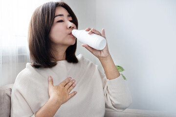 Asian woman taking antacid gel medicine to ease heartburn, stomach pain, and gas, showing common...