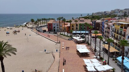 road on a beachside promenade with palm trees, volleyball nets, colorful buildings, and beachgoers