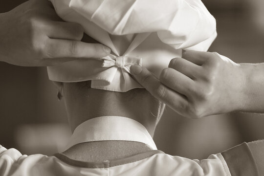 Fototapeta Сlose up of baker getting ready for work, tying ribbon of chef's hat, back view. Old black and white photo