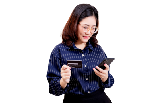 Asian young beautiful woman wearing glasses and a striped shirt is holding a credit card in one hand and a smartphone in the other, appearing to make an online payment.