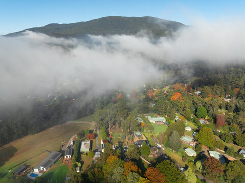 Aerial view of a rural town in a mountain valley with lingering clouds and colourful Autumn foliage