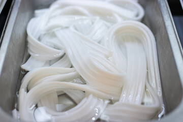 Fresh white flat rice noodles soaked in water, stored in a stainless steel tray for use in Asian hot pot, soup, or stir-fry dishes.