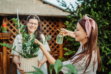 Two female friends or sisters taking care of plants with water can and mister	
