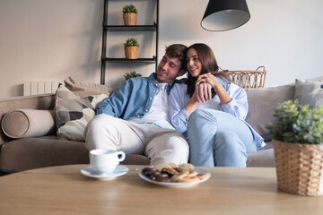 Young couple sitting on the sofa, smiling and talking peacefully together. Sharing dreams, planning...