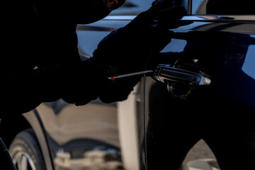 Criminal attempting to break into a parked car, highlighting risks of vehicle theft and security...