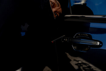 Criminal attempting to break into a parked car, highlighting risks of vehicle theft and security...