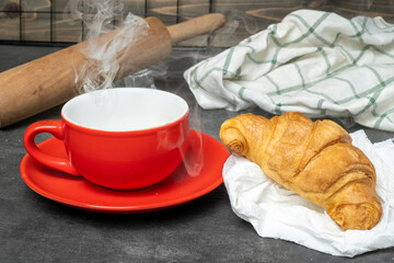 Cup of coffee and a freshly baked croissant with a rolling pin and a napkin on the table