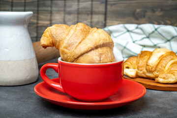 Freshly baked croissant in a cup of coffee with a rolling pin and a napkin on the table