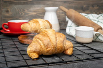 Freshly baked croissant and a cup of coffee with a rolling pin and a napkin on a cooling tray on the table