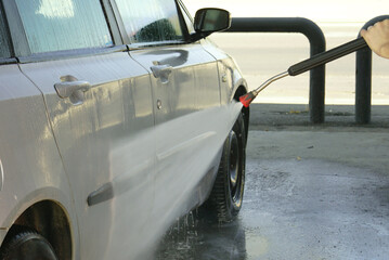 High pressure water jet washing dirty car body at self-service wash. Concept of transportation care, car maintenance, urban lifestyle, outdoor activity and saving money with DIY cleaning in summer