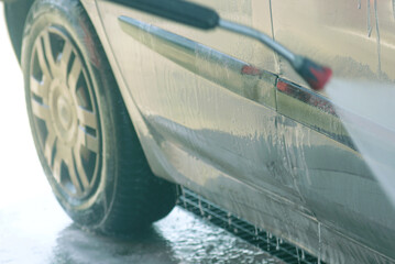 Close-up of car being washed with high pressure water at a self-service car wash station. Detail of water spraying on dirty vehicle body and tire. Transportation hygiene and eco-friendly DIY cleaning