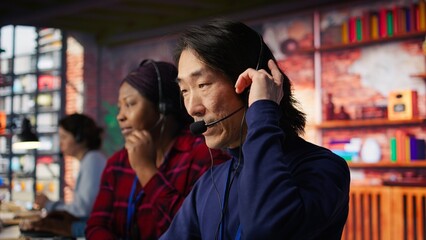 Customer center employee gesturing loud Asian senior agent to quiet down while working African...