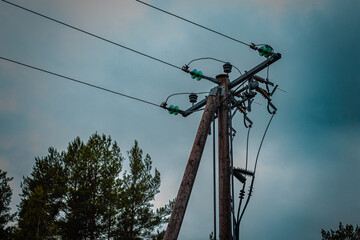 High-voltage wooden utility pole with insulators and power lines set against a cloudy sky and...