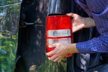 removing a headlight from a car to replace a bulb, man removing a rear brake light with his hands,...