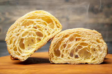 Closeup view slice of a freshly baked croissant on a wooden tray with a wooden background