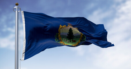 The state flag of Vermont waving on a flagpole against a blue sky.