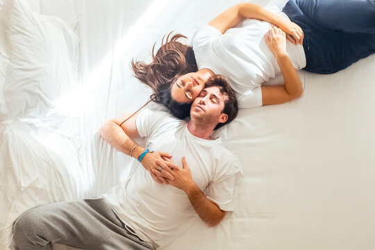 Young couple lying on the bed in casual homewear, smiling and talking about their future together. Happy and relaxed, planning life projects like marriage, living together, or building something meani - Powered by Adobe