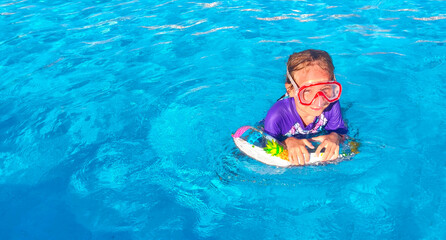 Little girl in a closed sleeved swimsuit, swimming mask and bright ring enjoys swimming in the pool in blue water on a hot summer day. Relax in the pool, hotel, travel with children
