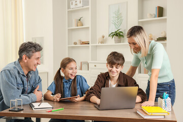 Fototapeta premium Happy parents and their children doing homework at table indoors