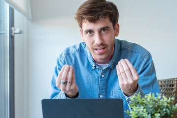 Confident young man sitting at desk with laptop, smiling and speaking directly to the camera....