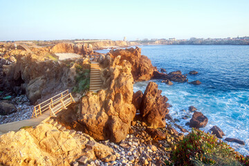 Sunny rocky coastline of Atlantic Ocean in the rays of setting sun, Papoa Island, Peniche, Portugal