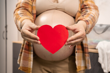 Pregnant woman holding red heart shape and feel love for unborn baby in belly. Awaiting for baby. Concept of maternity and pregnancy care