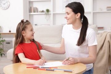 Mother teaching her daughter to draw at table indoors