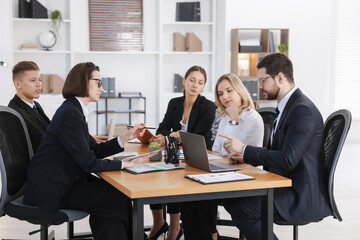 Coworkers with different devices working together at wooden table in office