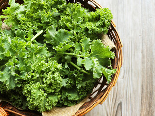 Top view of freshly harvested kale in a wicker basket on a rustic wooden background