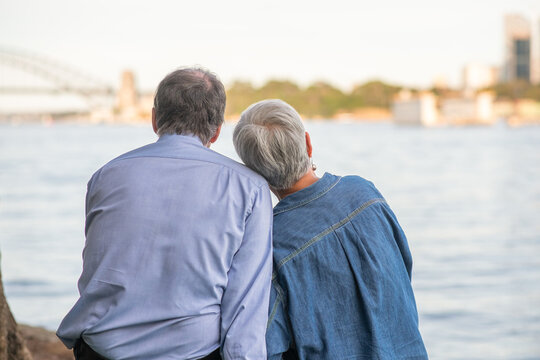 A senior couple sits side by side with their backs to the camera, enjoying the Sydney cityscape