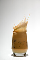 Iced caramel with ice cubes in a glass with a splash on a white background