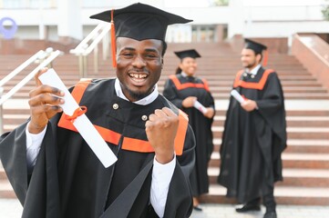 Happy graduate. Happy African man in graduation gowns holding diploma and smiling while his friends...