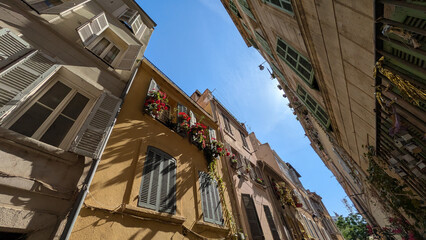 Looking up at colorful facades and open shutters with flowers, Le Panier, Marseille, France. Mediterranean architecture and vibrant summer atmosphere in historic city center